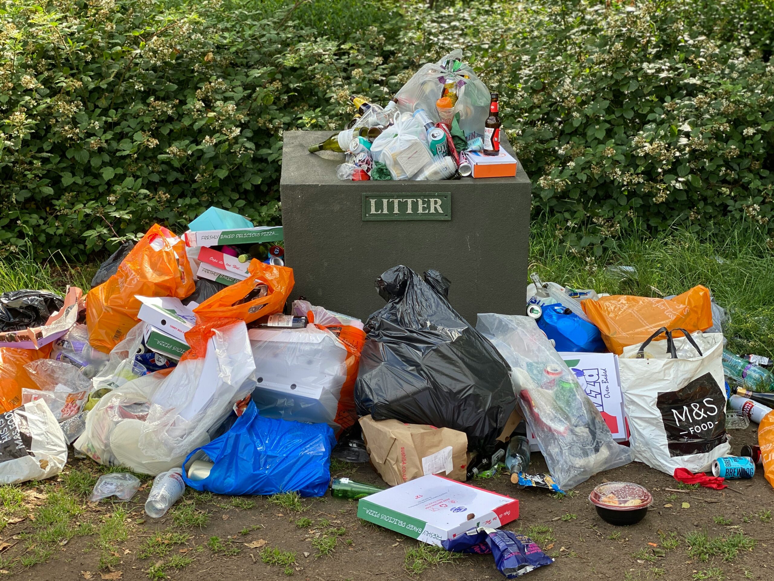 litter bin in park surrounded by rubbish.